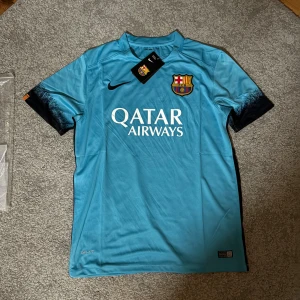 Blå FC Barcelona fotbollströja Nike - Snygg blå FC Barcelona fotbollströja från Nike med klubbmärke på bröstet och Qatar Airways-tryck på framsidan. Tröjan har svarta detaljer på ärmsluten och Unicef-tryck på ryggen. Tillverkad i lätt och ventilerande material, perfekt för träning eller match.