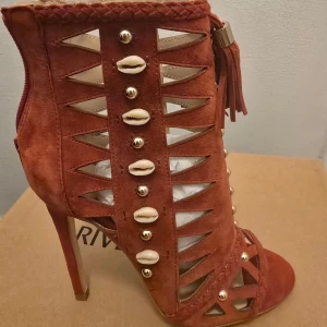 River Island röda mocka stövletter - Unika röda mocka stövletter från River Island med öppen tå, hög klack och snygga utskärningar. Skorna har dekorativa snäckor, guldfärgade nitar och tofsar upptill. Perfekt statement piece för dig som vill sticka ut.