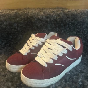 Vinröda sneakers med vita detaljer - Snygga vinröda sneakers med breda vita skosnören och vita detaljer på sidorna. Skorna är knappt användna!