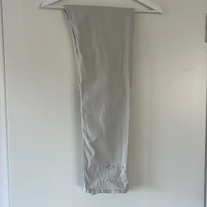 Ljusgrå chinos - Snygga ljusgrå chinos från Lindex i storlek 158. Klassisk rak passform med fickor bak och diskreta sömmar. Tillverkade i mjuk bomull som är skön att ha på sig. Perfekt för dig som gillar stilrena och enkla byxor. Liten defekt på ett av benen, en liten fläck som kanske går bort i tcätten, har inte testat. Därav priset.