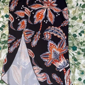 Blommig svart kjol med slits från SHEIN - Svart kjol från SHEIN med stort blommönster i orange, vitt och blått. Kjolen har en snygg slits framtill och är gjord i ett lätt och luftigt material. Perfekt för dig som gillar färgstarka prints och vill sticka ut lite extra.