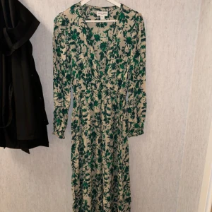 Blommig långklänning Holly & White  XS - Långklänning från Holly & White i beige med grönt blommönster. Klänningen har v-ringning, långa ärmar och markerad midja. Storlek Xs knappt använd 