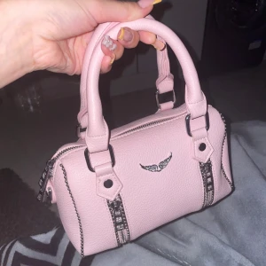 Ljusrosa handväska med silverdetaljer - Söt ljusrosa handväska som fåe plats med det man ska få plats med som tillkommer med ett långt band fortfarande inplastad, för fler bilder var god och skriv. Kan gå ner i pris vid snabb affär. SKRIV INNAN DU KÖPER TACK🩷EJ ÄKTA!!!