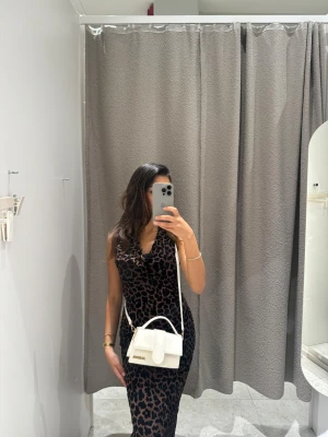 Svart leopardmönstrad långklänning - Säljer en svart långklänning med leopardmönster och v-ringad hals. Klänningen är ärmlös och har en slim passform som framhäver figuren. Perfekt för dig som vill sticka ut med ett djuriskt mönster och en elegant siluett. Klänningen är i XS