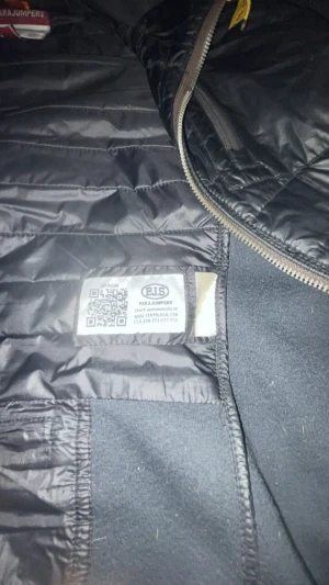 Svart quiltad jacka Parajumpers M - Svart jacka från Parajumpers med quiltad framsida och huva. Jackan har dragkedja, patch på ärmen och detaljer i gult. Materialmix med polyester och stickade partier på ärmar och sidor. Snygg och sportig look, perfekt för kyliga dagar.