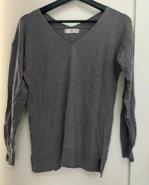 Grå v-ringad tröja från MNG - Grå v-ringad tröja från MNG med lång ärm och ribbade muddar. Tröjan har en loose passform och små slitsar i nederkanten. Perfekt för dig som gillar enkel och stilren design med en chill vibe.