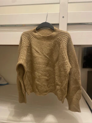 Beige stickad tröja från 157 - Stickad beige tröja från 157 med grov struktur och ribbad hög hals. Modellen har långa ärmar och breda muddar vid ärmslut och nederkant. Perfekt för dig som gillar chill och enkel stil under höst och vinter.