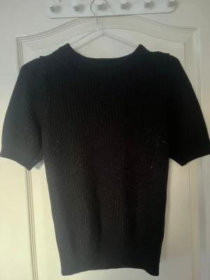 Svart stickad tröja Vero Moda - Svart stickad tröja från Vero Moda i storlek XS. Modellen har korta ärmar och rund halsringning, med ribbad struktur som ger en schysst och enkel look. Perfekt för dig som gillar stilrena och bekväma plagg.