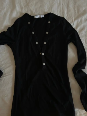 Svart långärmad topp från NA-KD - Svart långärmad topp från NA-KD med djup v-ringning och dekorativa silvriga knappar längs framsidan. Toppen är i ribbad bomull och har en slim passform som sitter snyggt på kroppen