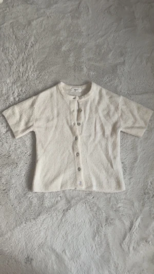 Vit ribbad kortärmad topp Gina Tricot - Superfin vit ribbad topp från Gina Tricot i ullblandning. Modellen har korta ärmar, rund hals och knappar.