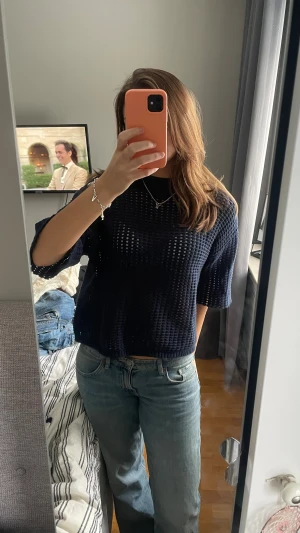 Mörkblå stickad topp med hålmönster - Säljer en mörkblå stickad topp med hålmönster och ribbad hög hals. Toppen har en loose passform och är kortärmad, vilket gör den superenkel att styla med jeans eller kjol. Materialet är mjukt och luftigt, perfekt för vår och sommar.