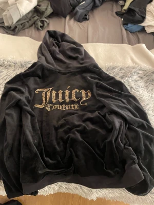 Svart Juicy Couture kofta/hoodie - Svart hoodie från Juicy Couture i mjuk velour med strassdetaljer på bröstet och stor Juicy Couture-logga i strass på ryggen. Tröjan har huva, dragkedja i guld och fickor framtill. Perfekt för dig som gillar klassisk Y2K-stil. Jag har själv inte använt den så mycket, har legat i garderoben ett tag. Nypris över 1000, mitt pris kan självklart diskuteras!🥰 fler bilder kan skickas om så önskas