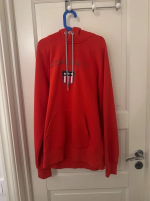 Röd Gant Hoddie - Säljer en röd hoodie från GANT i storlek S. Tröjan har huva med snörning, stor magficka och broderad GANT-logga med sköld på bröstet. Mjuk och skön, perfekt för chill dagar. Långärmad och med klassisk passform.