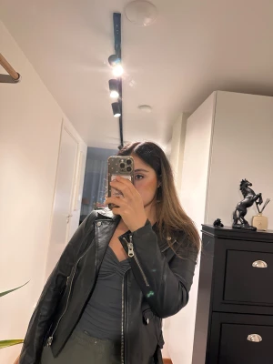 Svart skinnjacka med bälte, Jofama M - Säljer en svart skinnjacka från Jofama i storlek M. Jackan har klassisk bikerstil med flera dragkedjor, fickor och ett bälte i midjan. Snygg passform och detaljer i silverfärg. Perfekt för dig som vill ha en edgy look.