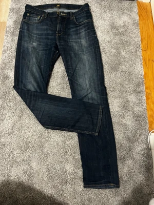 Mörkblå Lee jeans straight fit - Snygga mörkblå jeans från Lee med klassisk straight fit och kontrasterande gula sömmar. Modellen har fem fickor, Lee-logga på bakfickan och läderpatch i midjan. Jeansen är tillverkade i slitstarkt denim och har dragkedja och knapp framtill.