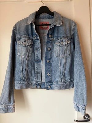 Blå jeansjacka från Acne Studios - Säljer en klassisk blå jeansjacka från Acne Studios Blå Konst. Jackan har raka linjer, två bröstfickor med lock och knappar framtill. Tillverkad i 100% bomull med snygg tvättad finish och coola detaljer. Perfekt för dig som gillar stilren och tidlös denim.