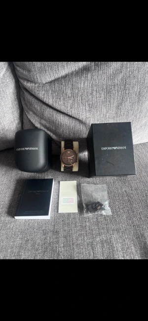 Emporio Armani brun/guld klocka - Snygg Emporio Armani AR-5890 klocka med rund urtavla i brunt och detaljer i guld. Länkarmband i mörkbrunt rostfritt stål. Kommer med originalask, certifikat och extra länkar. Perfekt accessoar för dig som gillar stilrena och lyxiga detaljer.