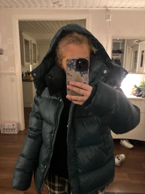 Mörkgrön pufferjacka med huva - Säljer en mörkgrön pufferjacka med stor huva och dragkedja framtill. Jackan är quiltad och har långa ärmar samt praktiska fickor med knappstängning. Perfekt för kalla dagar och riktigt skön att bära. Säljer inte för under 1000💗