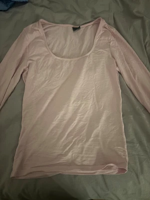 Ljusrosa långärmad topp med slits - Säljer en ljusrosa långärmad topp med rundad, djup urringning och slitsdetalj vid ärmslut. Toppen är i mjuk bomull och har en slim passform som sitter snyggt på kroppen. Perfekt för dig som gillar enkla och stilrena plagg.