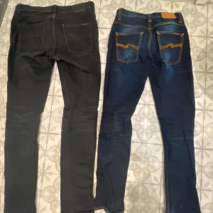 Två pack Nudie jeans - Två par jeans från Nudie, ett par svarta och ett par mörkblå med kontrastsömmar och klassiska Nudie-detaljer på bakfickorna. Båda har smal passform och raka ben, tillverkade i slitstarkt denim. Jeansen är i storlek 31/34 och är otroligt snygga.