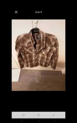 Brun rutig skjorta från KappAhl - Snygg brun rutig skjorta från KappAhl med klassisk krage och knappar framtill. Skjortan har långa ärmar och två bröstfickor med lock. Perfekt för dig som gillar en avslappnad och cool stil.