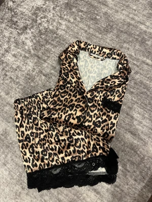 Leopardmönstrade satinshorts med spets - Snygga leopardmönstrade shorts i satin med svart spetskant. De har en loose passform och elastisk midja för extra komfort. Perfekta för dig som gillar att sticka ut med djurmönster och mjuka material. Passar till chill hemma eller som pyjamas.