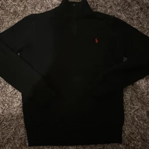 Svart stickad half zip från Polo Ralph Lauren - Svart stickad tröja från Polo Ralph Lauren med röd broderad logga på bröstet. Tröjan har half zip i halsen och långa ärmar. Perfekt för lager-på-lager och snygg till jeans eller chinos.
