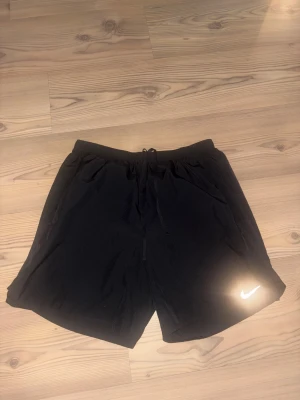 Svarta Nike Dri-Fit träningsshorts - Svarta Nike Dri-Fit shorts med elastisk midja och snörning. Lätta och luftiga med klassisk Nike-logga i vitt på benet. Perfekta för träning eller sportiga dagar. Tillverkade i funktionsmaterial som andas och transporterar bort fukt.