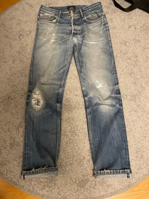 Selvedge jeans från A.P.C.  - Snygga blå jeans från A.P.C. med coola slitningar och distressed detaljer på benen. Klassisk femficksmodell med selvedge-kant vid benslut. Jeansen har rak passform och är tillverkade i robust bomullsdenim. Perfekt för dig som gillar en avslappnad och trendig look.