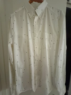 Vit skjorta med myr-mönster East West - Vit skjorta från East West köpt på Wolt i slim fit med svarta myror. Klassisk krage, bomullstyg och bröstficka.