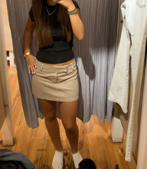 Beige kortkjol med bälteshällor - Stilren beige kortkjol med raka linjer och bälteshällor i midjan. 