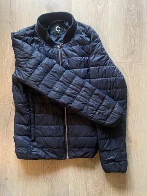 Mörkblå lättviktsjacka, Cubus - 100% polyester. Fyllning: 90% dun, 10%fjädrar  Tvättråd: 40°