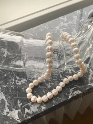 Klassiskt pärlhalsband med vita pärlor - Säljer ett elegant pärlhalsband med runda, vita pärlor som har en fin lyster. Halsbandet har ett diskret silverspänne (925 stämpel) och pärlorna är jämnt placerade längs hela bandet. Perfekt för dig som gillar tidlös och stilren design.