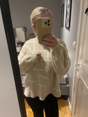 Beige fluffig stickad tröja med mönster - Supermysig beige stickad tröja med vitt grafiskt mönster. Tröjan har en loose passform, långa ärmar och är gjord i ett fluffigt material som känns extra skönt mot huden. Perfekt för dig som gillar oversized och chill vibe.
