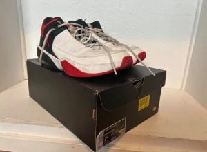 Nike Air Jordan Max Aura 3 - Nike Jordan sneakers med en clean design i vitt, svart och rött. Skorna har snörning, platt sula och rund tå. Ovandelen är i skinn med röda detaljer och klassisk Jumpman-logga på sulan. Perfekt för dig som gillar streetstyle och basketinspirerat mode. Crease-skydd är använt.