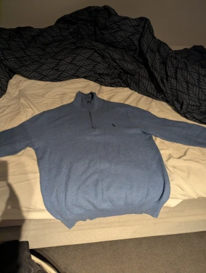 Blå polotröja från Ralph Lauren - Snygg blå polotröja från Ralph Lauren med half zip och diskret broderad logga på bröstet. Tröjan har lång ärm och är tillverkad i mjuk bomull, perfekt för dig som gillar klassisk stil med en modern touch. Knappt använd klpt för 2400