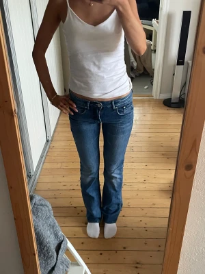 Blå jeans från Star med fjärilar - Snygga blå jeans från Star med låg midja och bootcut-snitt. Baktill finns broderade fjärilar på fickorna som ger en unik och cool vibe. Jeansen har klassisk femficksdesign och är gjorda i slitstarkt denim. Perfekt för dig som gillar detaljer och vill sticka ut.