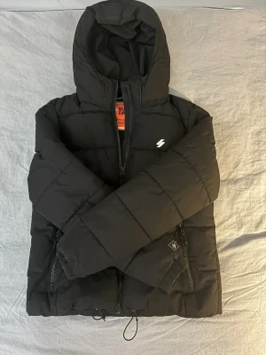 Svart pufferjacka från Superdry M - Svart pufferjacka från Superdry MTN Sports Puffer Series. Jackan har huva, dragkedja framtill och två sidofickor med dragkedja. Broderad logga på bröstet och detaljer på ärmen. Perfekt för kalla dagar och riktigt snygg stil. Nypris:1000kr Mitt pris:499kr