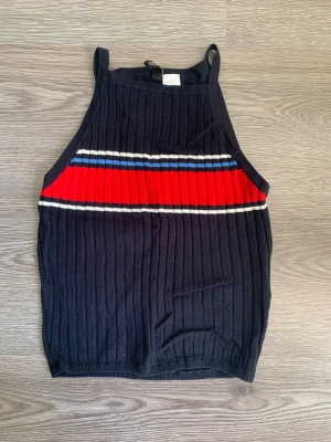Randig ribbad linnetopp från H&M - Säljer en mörkblå ribbad linnetopp från H&M i storlek S. Toppen har tunna axelband och ett randigt mönster med röd, vit och blå horisontella ränder över bröstet. Materialet är mjukt och stretchigt, perfekt för en chill och sportig look.