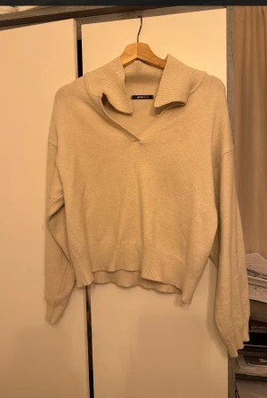 Beige stickad tröja Gina Tricot - Snygg beige stickad tröja från Gina Tricot med bred krage och v-ringning. Tröjan har långärmade ärmar och ribbade detaljer vid kragen och muddar. Perfekt för dig som gillar en chill och stilren look. Men funkar även som S och M