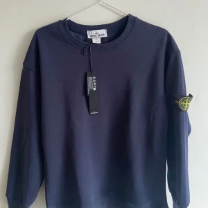 Mörkblå sweatshirt från Stone Island - Säljer en stilren mörkblå sweatshirt från Stone Island med klassisk rund hals och ribbade muddar. Tröjan har den ikoniska loggan på ärmen och är tillverkad i mjuk bomull även mjukt lurv inuti. Perfekt för dig som gillar streetwear och vill ha en clean look. Skriv gärna vid fårågor! 