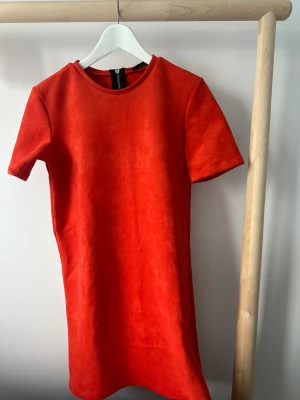 Kortklänning från Zara - Klänning från Zara med rund hals och korta ärmar. Klänningen har en rak passform och är tillverkad i mjuk syntet med mockakänsla. Dragkedja baktill för enkel påklädning. 