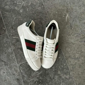 Gucci ace  - Säljer ett par klassiska vita Gucci sneakers i skinn med gröna och röda ränder på sidan. Storlek 42 och skicket är i princip nytt. Dessa är äkta till skillnad från många andra och allt og tillkommer. Orderbekräftelse finns. 