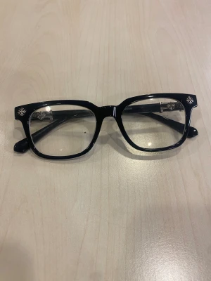 Chrome Hearts - Snygga svarta glasögon med rektangulär form och coola silverfärgade detaljer på bågarna. Kommer med mintgrönt fodral och putsduk. Bågarna har en stilren look med metallinslag vid gångjärnen och små blommor i hörnen för extra vibe. (Pris går att diskutera!!!)