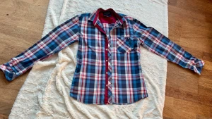 Rutig Bondelid skjorta i blå och röd - Snygg rutig skjorta från Bondelid i storlek Small. Skjortan har ett klassiskt mönster i blått, rött och vitt, med en bröstficka och knappar framtill. Materialet är mjuk bomull och insidan av kragen är röd. Perfekt för dig som gillar en chill och stilren look.