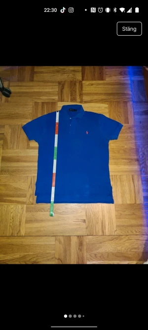 Blå pikétröja från Polo Ralph Lauren - Blå pikétröja från Polo Ralph Lauren i storlek M. Klassisk design med krage, korta ärmar och knappar framtill. Tröjan har den ikoniska röda Polo-loggan broderad på bröstet och är tillverkad i mjuk bomull. Perfekt för en clean och sportig look. Kostar ca 1500kr ny!