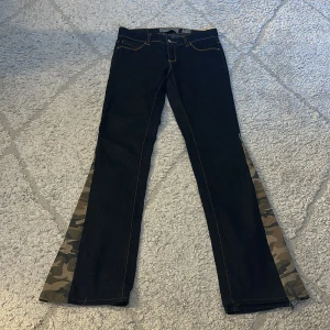 Jeans med camouflage-detaljer från Vero Moda - Unika jeans från Vero Moda med raka ben och camouflage-tyg i utsvängda benslut. Mörkblå denim med kontrastsömmar och klassisk femficksdesign. Perfekta för dig som vill sticka ut med en cool twist på klassiska jeans. Jag har sytt om dom själv och även sytt upp dom