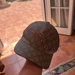 Gucci keps med orm och GG-mönster - Snygg keps från Gucci med klassiskt GG-monogram i beige och brunt, prydd med en röd och vit orm på framsidan. Baksidan är i svart mesh för extra ventilation och justerbar passform. Perfekt statement-piece för dig som vill sticka ut. Nypris ca 4500kr  tar byte 