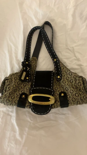 Vintage Guess axelväska - Snygg vintage axelväska från Guess med monogram mönster. Svår att få tag på, perfekt för dig som gillar vintage 2000s mode. 
