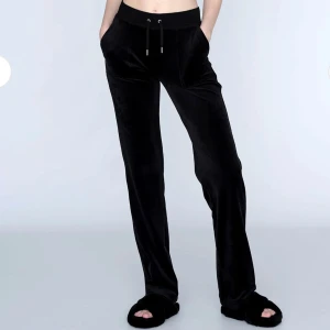 Svarta juicy couture byxor - Svarta juicy couture byxor i mjukt sammetstyg. Byxorna har resårmidja med snörning, stora fickor fram och bak med knappdetaljer. Perfekta för chill dagar och har en stilren look.